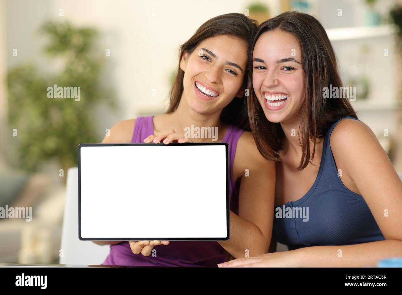 Zwei lustige Frauen, die zu Hause auf dem leeren Tablet-Bildschirm der Kamera zu sehen sind Stockfoto