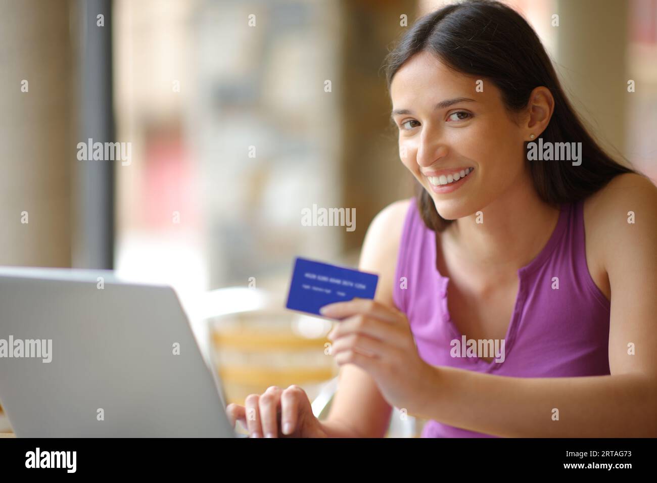 Happy Woman schaut auf die Kamera, die online mit Kreditkarte und Laptop auf einer Bar-Terrasse kauft Stockfoto