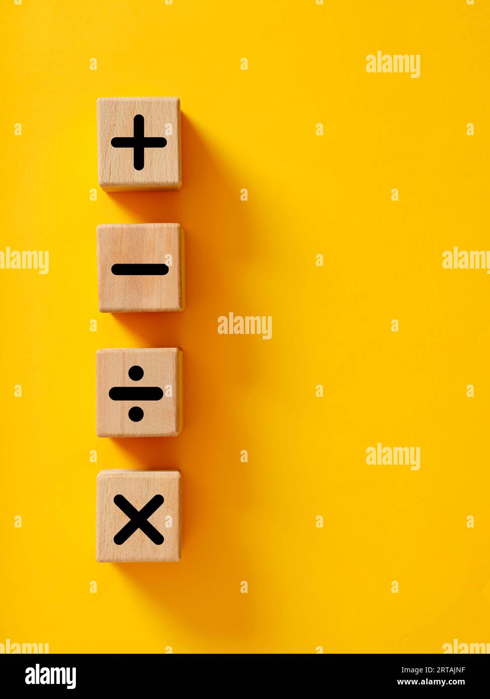 Symbole für grundlegende mathematische Operationen. Plus, Minus, Multiplikation und Teilung von Symbolen auf Holzwürfeln auf gelbem Hintergrund. Mathematik- oder Mathematikunterricht und Stockfoto