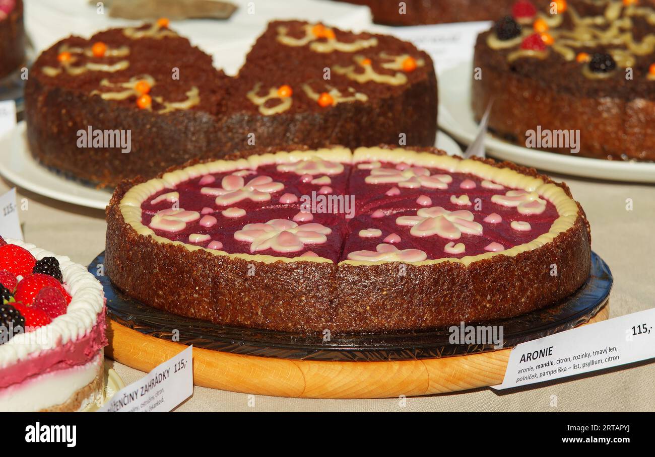 Konditorstand mit Variationen von nicht gebackenen ROHEN Kuchen, Aronia oder auch Apfelbeerkuchen mit Mandelnüssen im Vordergrund, Nahaufnahme ohne Leute bei farme Stockfoto