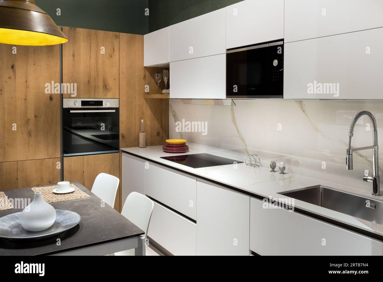 Inneneinrichtung der modernen Küche, die renoviert wird, mit weißen Schränken, Waschtisch, Wasserhahn, Herd mit Geräten, Ofen und Essbereich mit Tisch Stockfoto