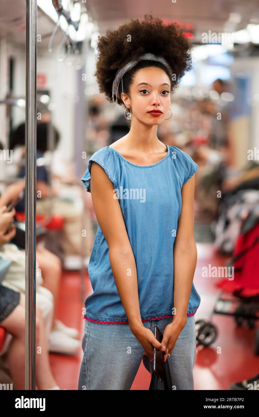 Stilvolle junge gemischte Rasse weibliche Millennials mit dunklen Afro-Haaren und roten Lippen in lässigem Outfit, die Kamera beim Stehen in der U-Bahn mit sma Stockfoto