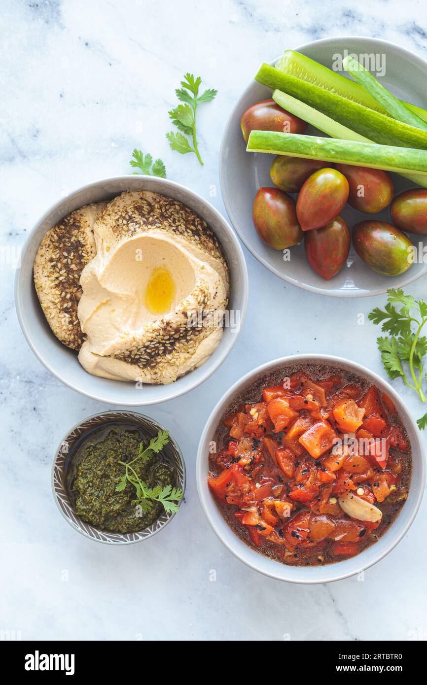 Vegetarische Vorspeisen: Hummus, gebratener Paprikasalat, Pesto und frisches Gemüse, Blick von oben. Veganes Lebensmittelkonzept. Stockfoto