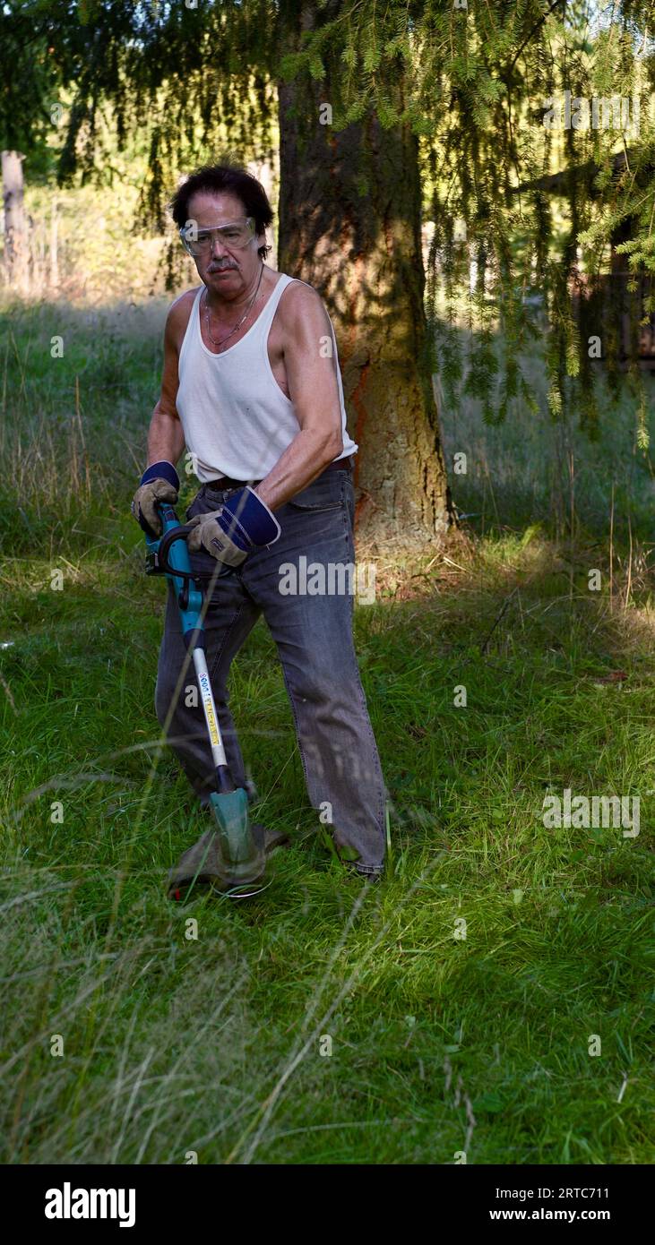 Mann mäht Gras mit einem elektrischen Schnur-Trimmer. Stockfoto