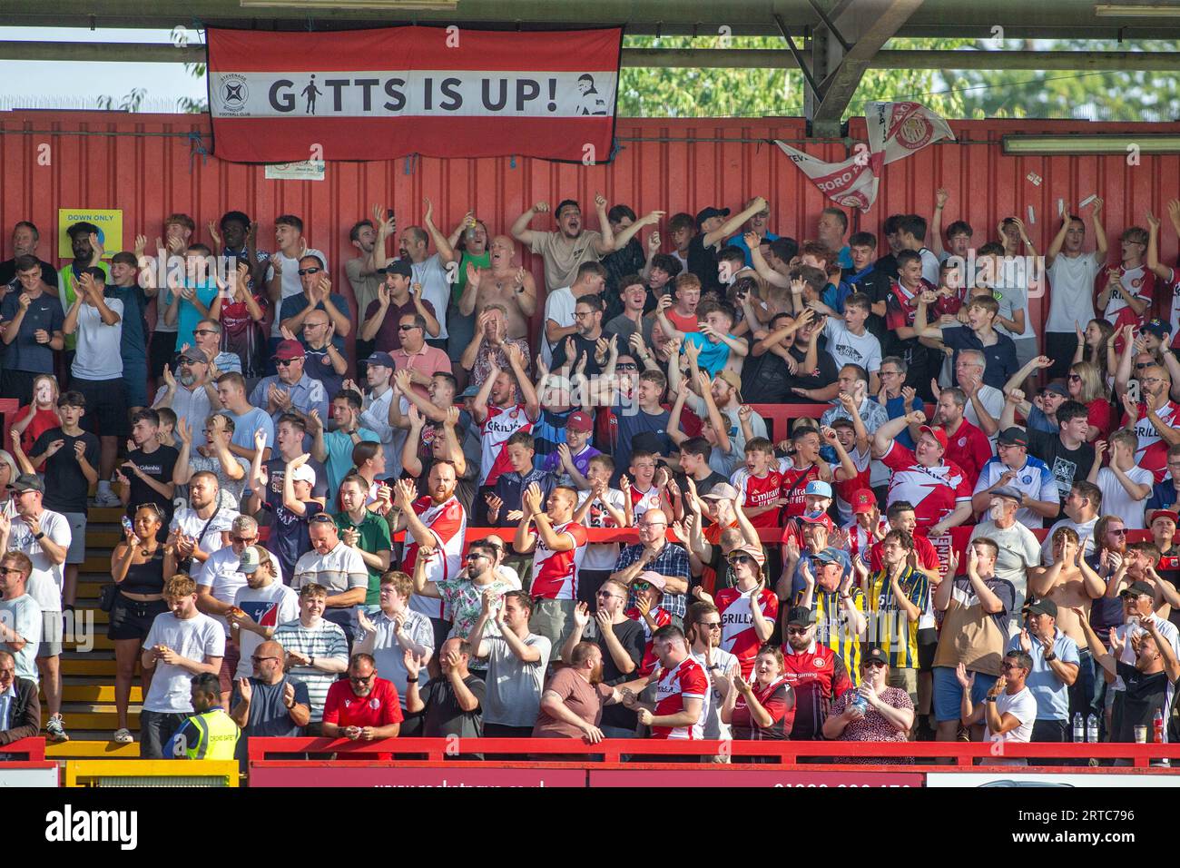 Fußballfans singen, singen und feiern auf der Stehterrasse im Lamex Stadium, dem Heimstadion des Stevenage FC Stockfoto