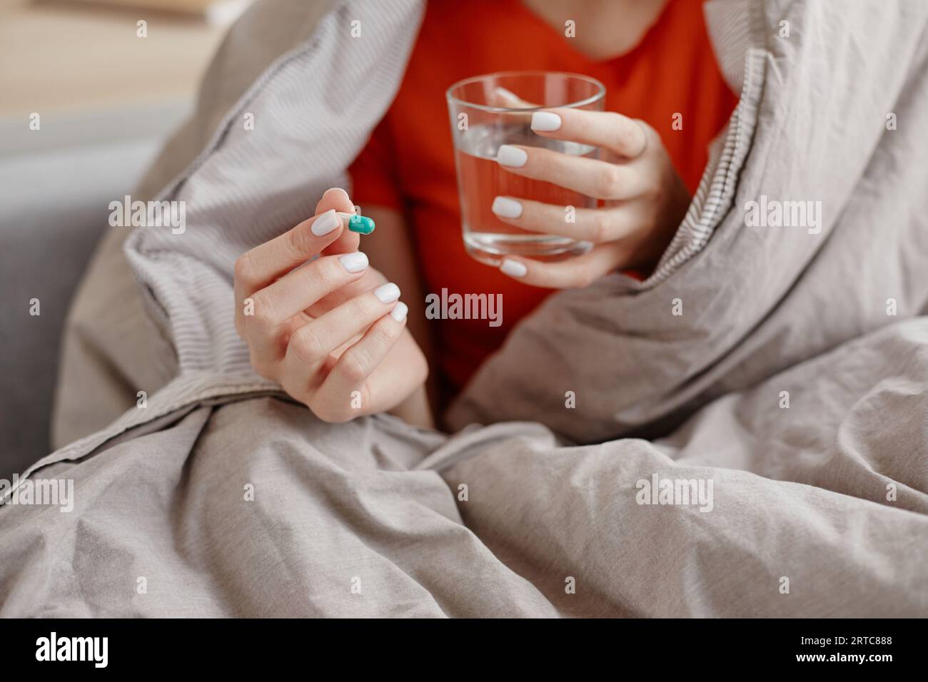 Nahaufnahme einer jungen Frau, die Pille und ein Glas Wasser in Decke, Kopierraum hält Stockfoto