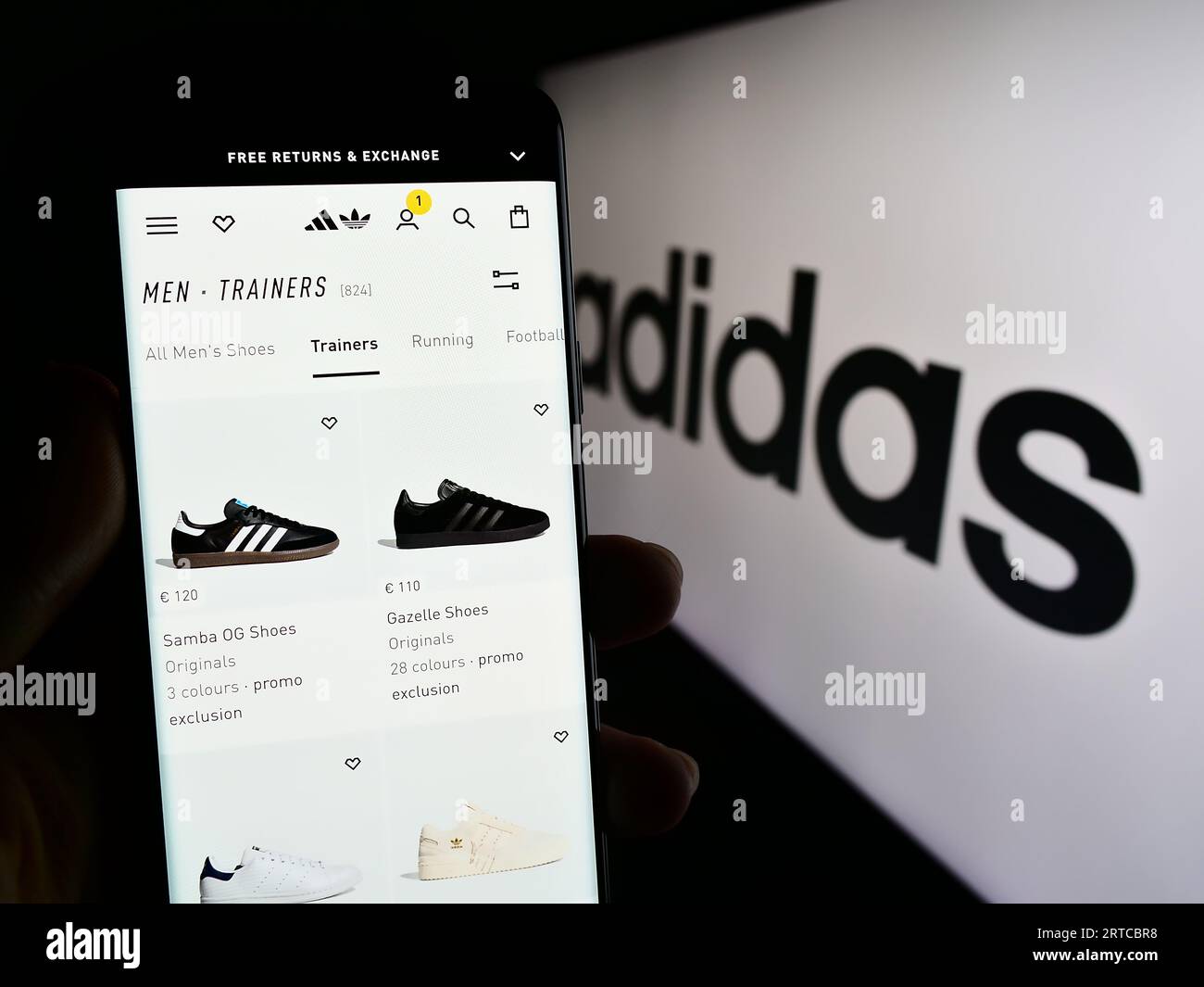 Person, die ein Mobiltelefon mit Webseite des deutschen Bekleidungs- und Schuhherstellers Adidas AG auf dem Bildschirm mit Logo hält. Konzentrieren Sie sich auf die Mitte der Telefonanzeige. Stockfoto