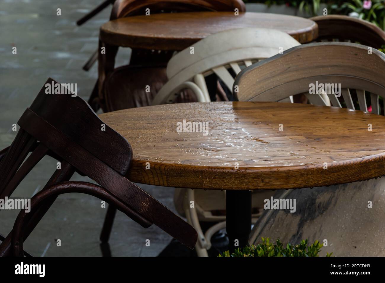 Leere nasse Holztische und -Stühle auf der Terrasse der Cafeteria im Freien bei Regen. Straßenleben im Regen. Stockfoto