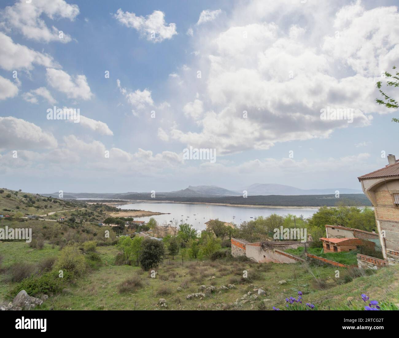 Schöner Panoramablick auf eine grüne Landschaft im Frühjahr mit dem Atazar-Stausee im Hintergrund. Es liegt im Dorf El Berrueco. Stockfoto