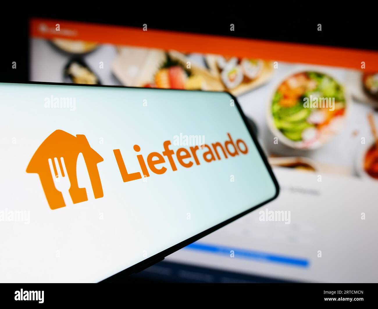Handy mit Logo des deutschen Lebensmittellieferanten Lieferando auf dem Bildschirm vor der Business-Website. Fokus auf der linken Seite des Telefondisplays. Stockfoto