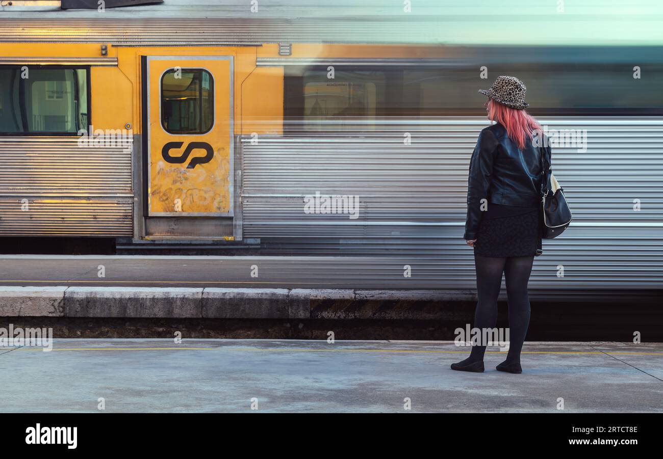 Die Frau wartet auf dem Bahnsteig, während ein fahrender Zug an einem stationären vorbeifährt Stockfoto