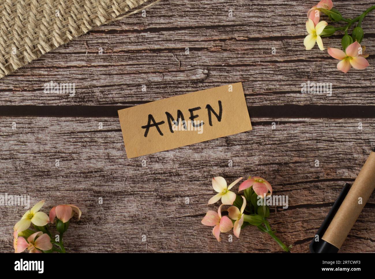 Amen, handgeschriebener Text mit englischen Großbuchstaben auf einem Holztisch mit Blumen und Stift im Vintage-Stil. Draufsicht, flach. Stockfoto