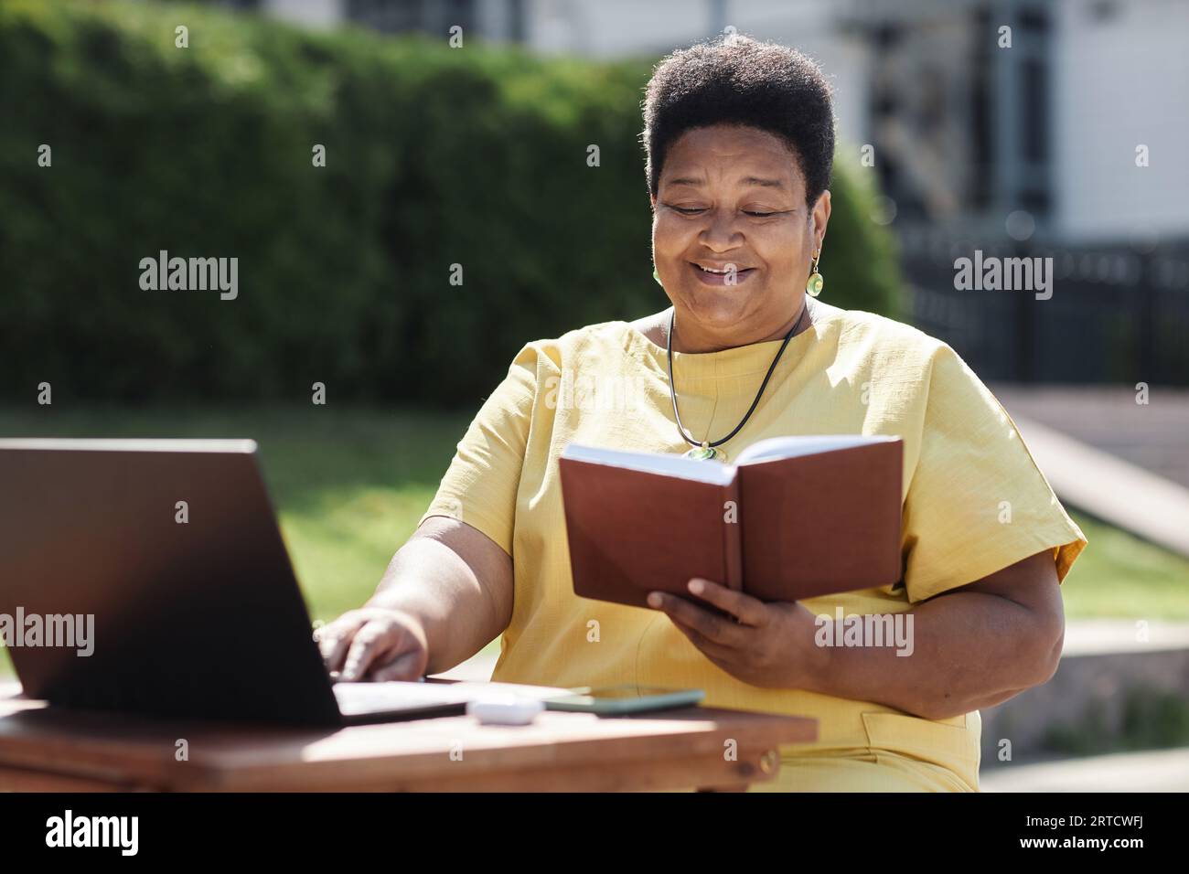 Porträt der lächelnden Schwarzen Seniorfrau, die im Sonnenlicht draußen Buch liest Stockfoto