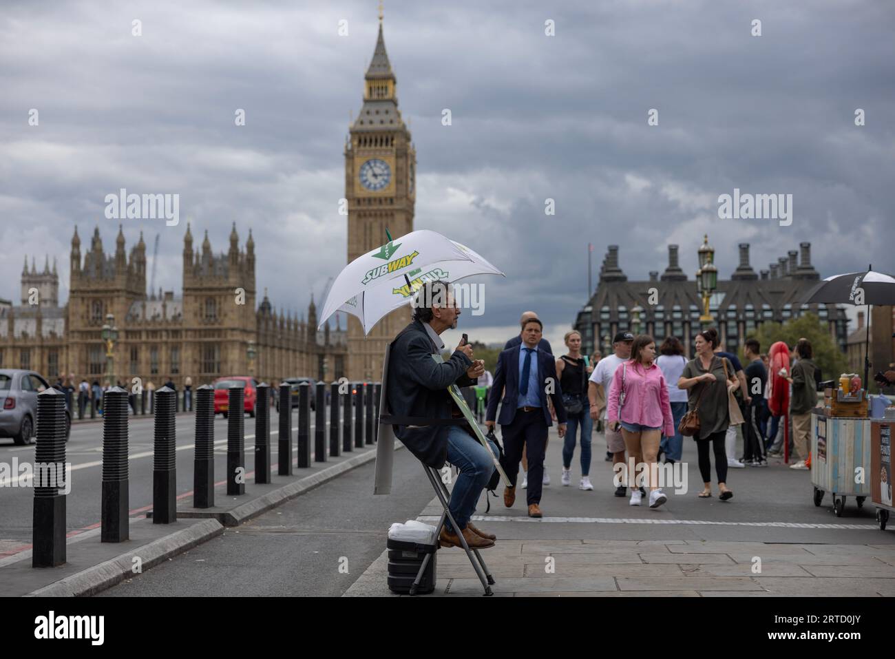 Ein Mann sitzt auf einem Klappstuhl und wirbt für und gibt Wegbeschreibungen zum U-Bahn-Fast-Food-Restaurant, Westminster Bridge, London, England, Großbritannien Stockfoto