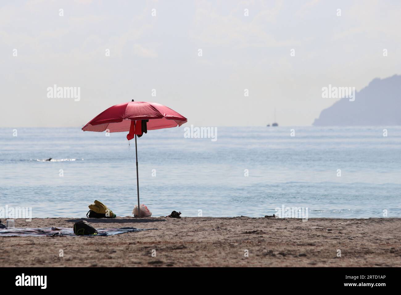 Blick auf einen Sandstrand mit einem roten Sonnenschirm, einige Badeutensilien, das silbergraue Meer und den Horizont, Kopierraum Stockfoto