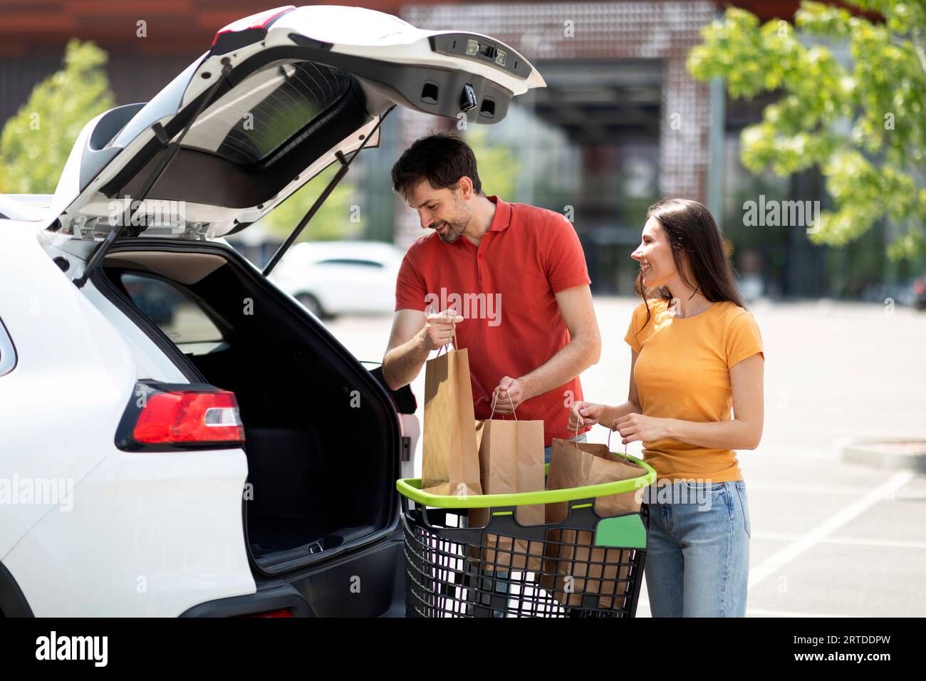 Glückliches Millennials-Paar, das Einkäufe nach dem Einkaufen in den Kofferraum lädt Stockfoto