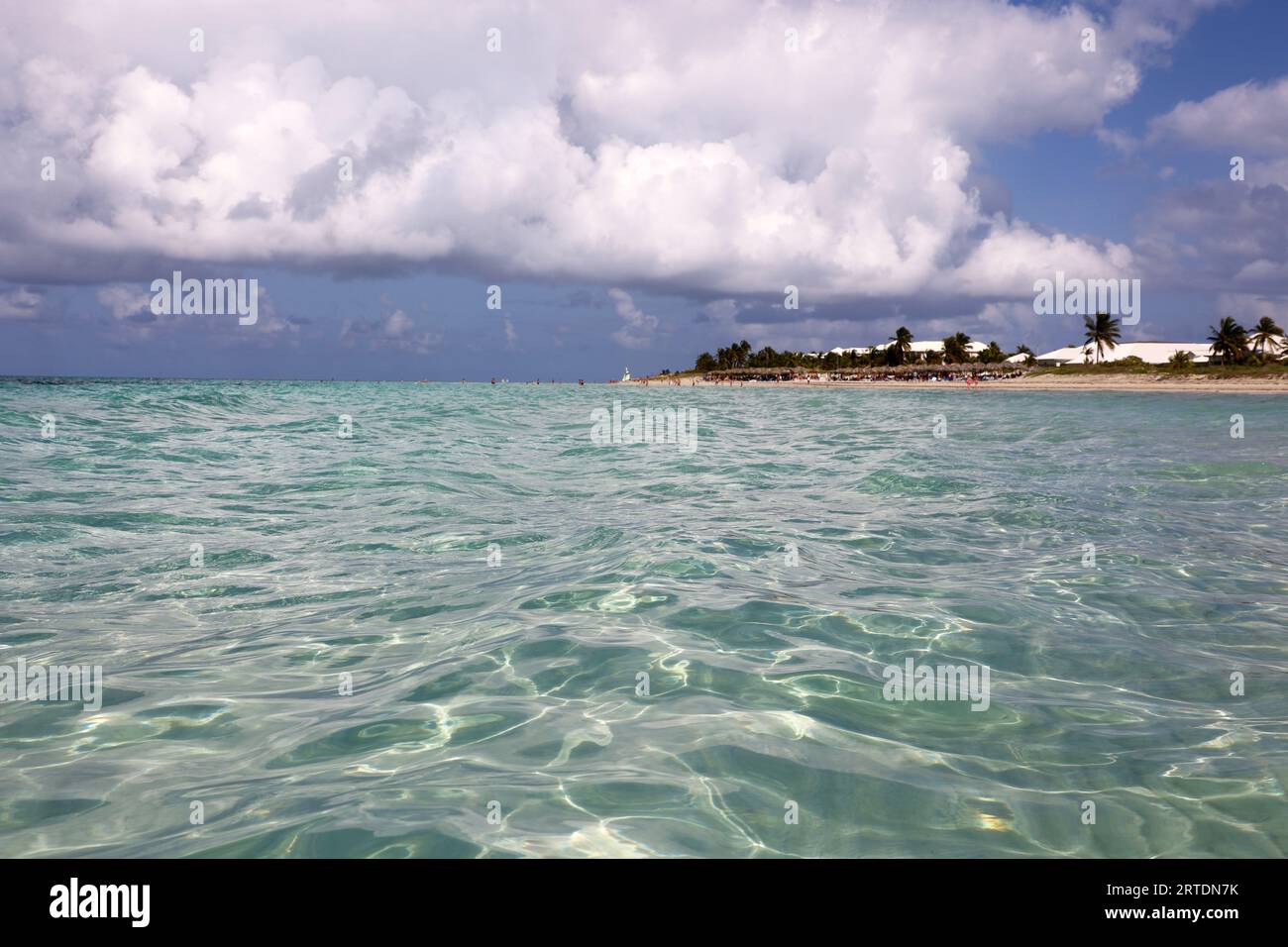 Blick von der Meeresoberfläche zum tropischen Strand mit Menschen, Sandküste und Kokospalmen. Seebad auf Karibikinsel mit klarem Wasser Stockfoto