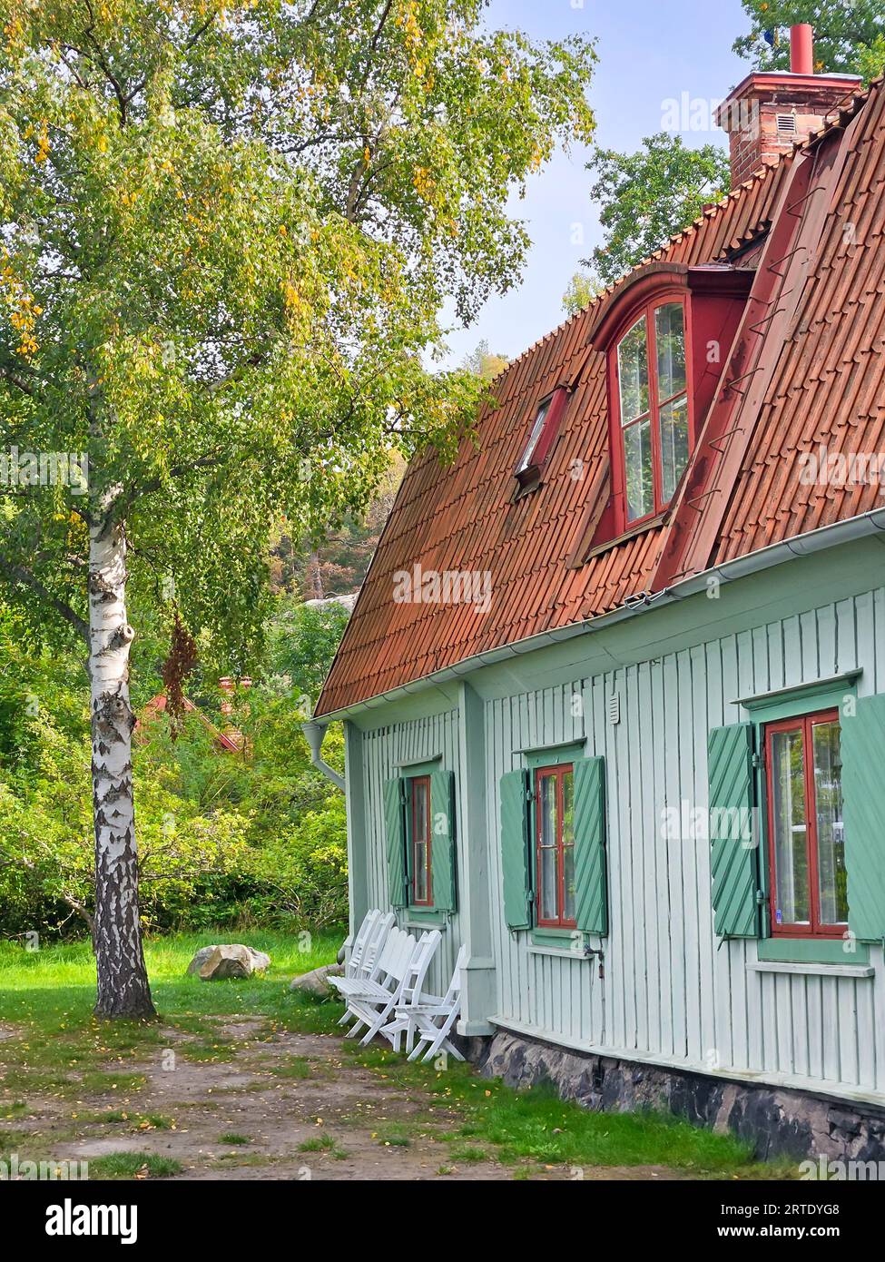 Rustikales altes hellblaues Holzhaus mit Ziegeldach auf schwedischem Land mit Birke im grünen Garten mit gelben Blättern im Frühherbst Stockfoto