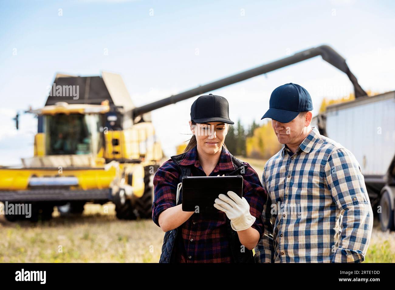 Nahaufnahme eines Mannes und einer Frau, die ein tragbares drahtloses Gerät zur Verwaltung und Überwachung ihrer Rapsernten verwenden, während der Mähdrescher Getreide in... Stockfoto