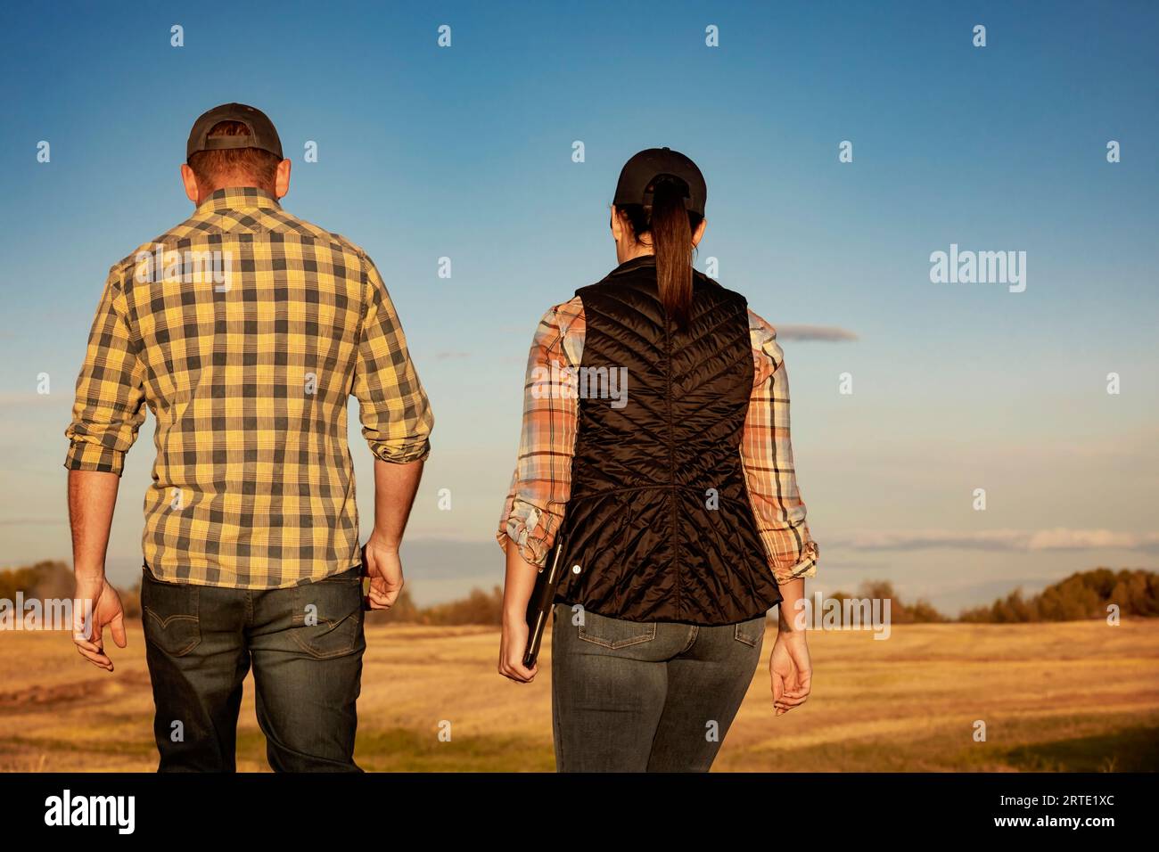 Ein Blick von hinten auf einen Mann und eine Frau, die auf einem ernteten Feld spazieren und nach Abschluss ihrer Rapsernte einige Zeit miteinander verbringen Stockfoto