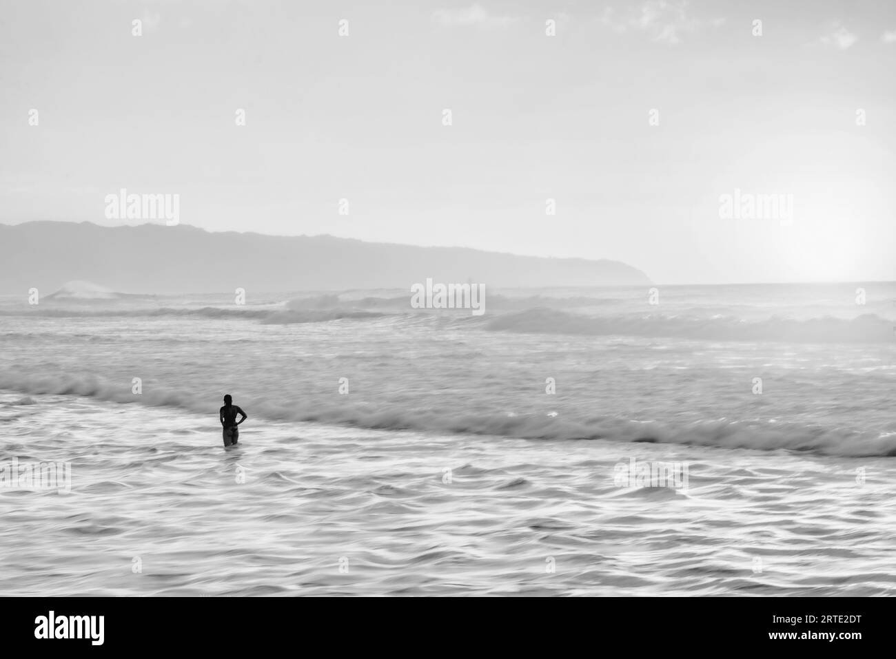 Silhouettenfrau steht im Wasser und beobachtet die Wellen des Ozeans Stockfoto