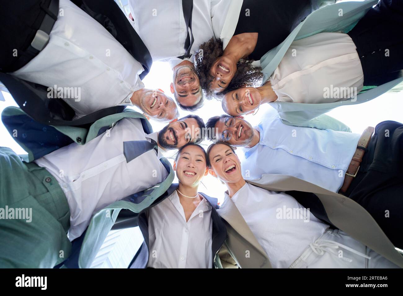 Multirassische, vielfältige Gruppenbüros Männer Frauen Kollegen, die sich im Kreis umarmen und die lächelnde Kamera nach unten schauen. Stockfoto