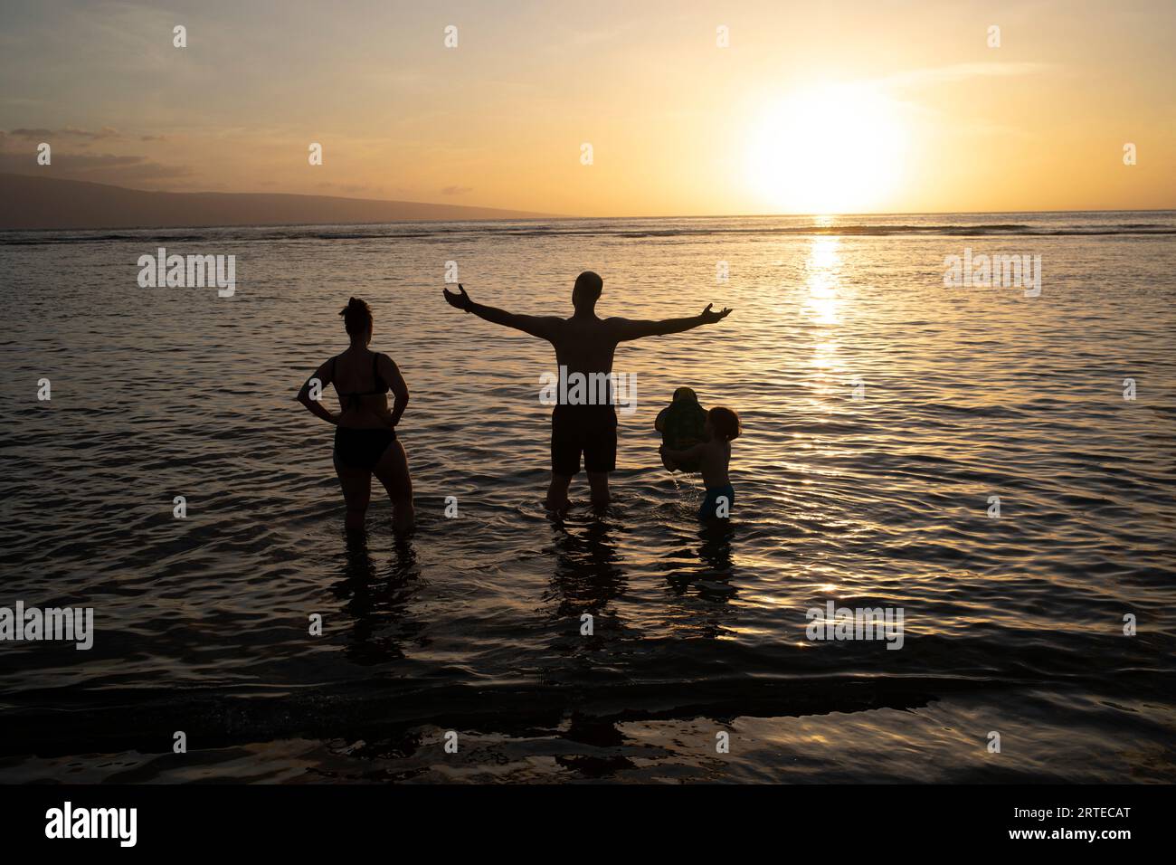 Blick von hinten auf eine Silhouette einer Familie, die in der Dämmerung im Wasser steht und die Natur genießt Stockfoto