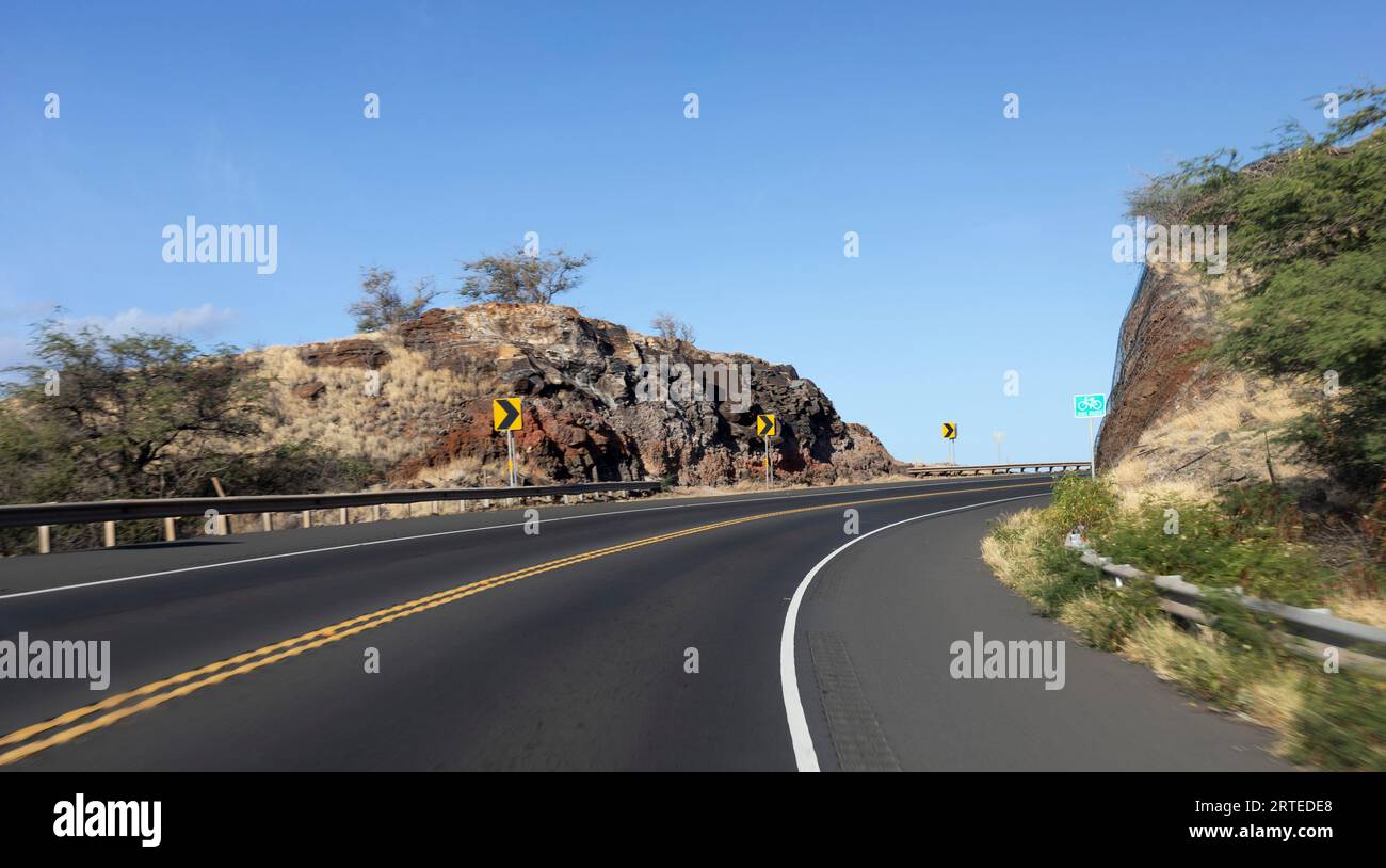 Gepflasterte Autobahn mit scharfen Kurven in der Straße durch die felsigen Klippen an einem Berghang mit blauem Himmel; Maui, Hawaii, Vereinigte Staaten von Amerika Stockfoto