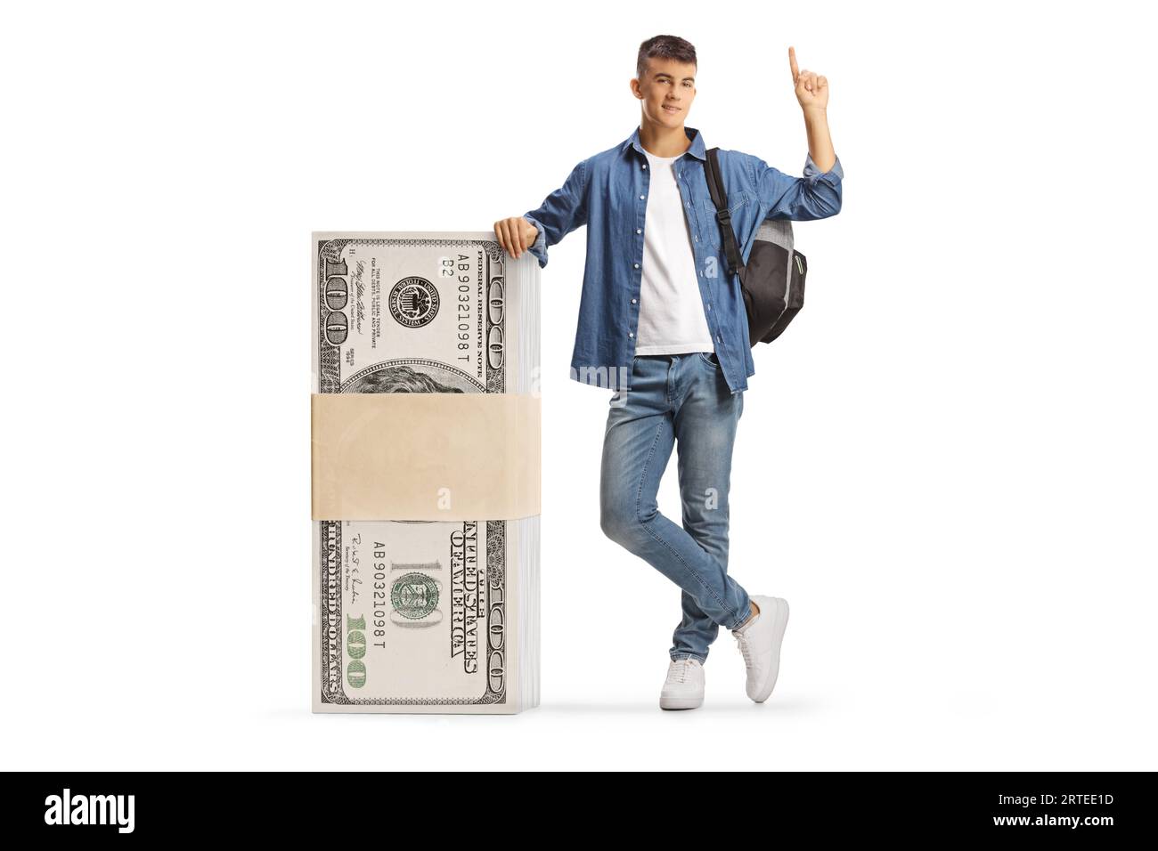 Männlicher Student, der sich auf einen Stapel von US-Dollar-Banknoten lehnt und isoliert auf weißem Hintergrund nach oben zeigt Stockfoto