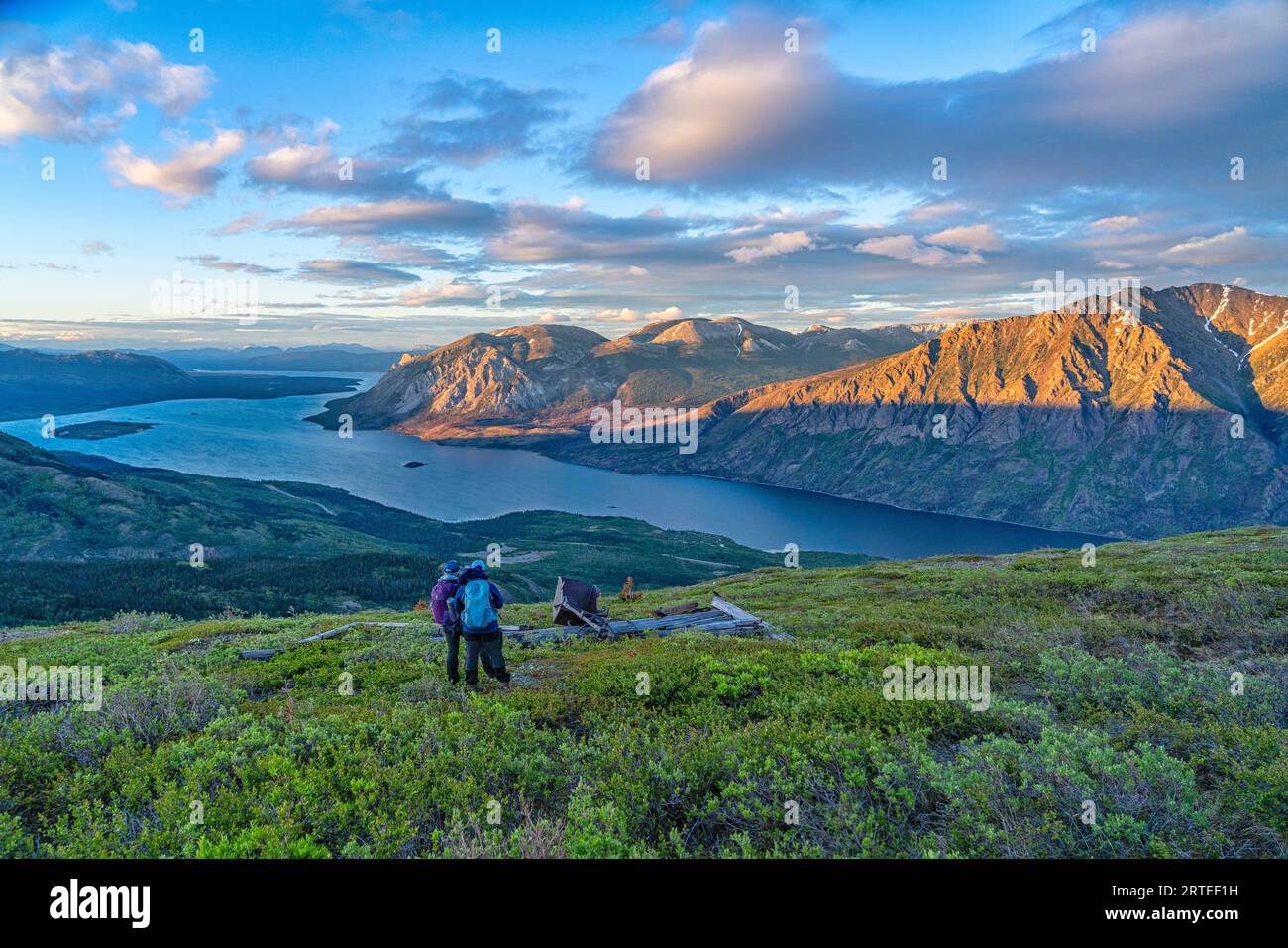 Blick von hinten auf zwei Frauen, die auf einem Berggipfel mit Armen um die Schultern stehen, die Aussicht genießen, während sie die... Stockfoto