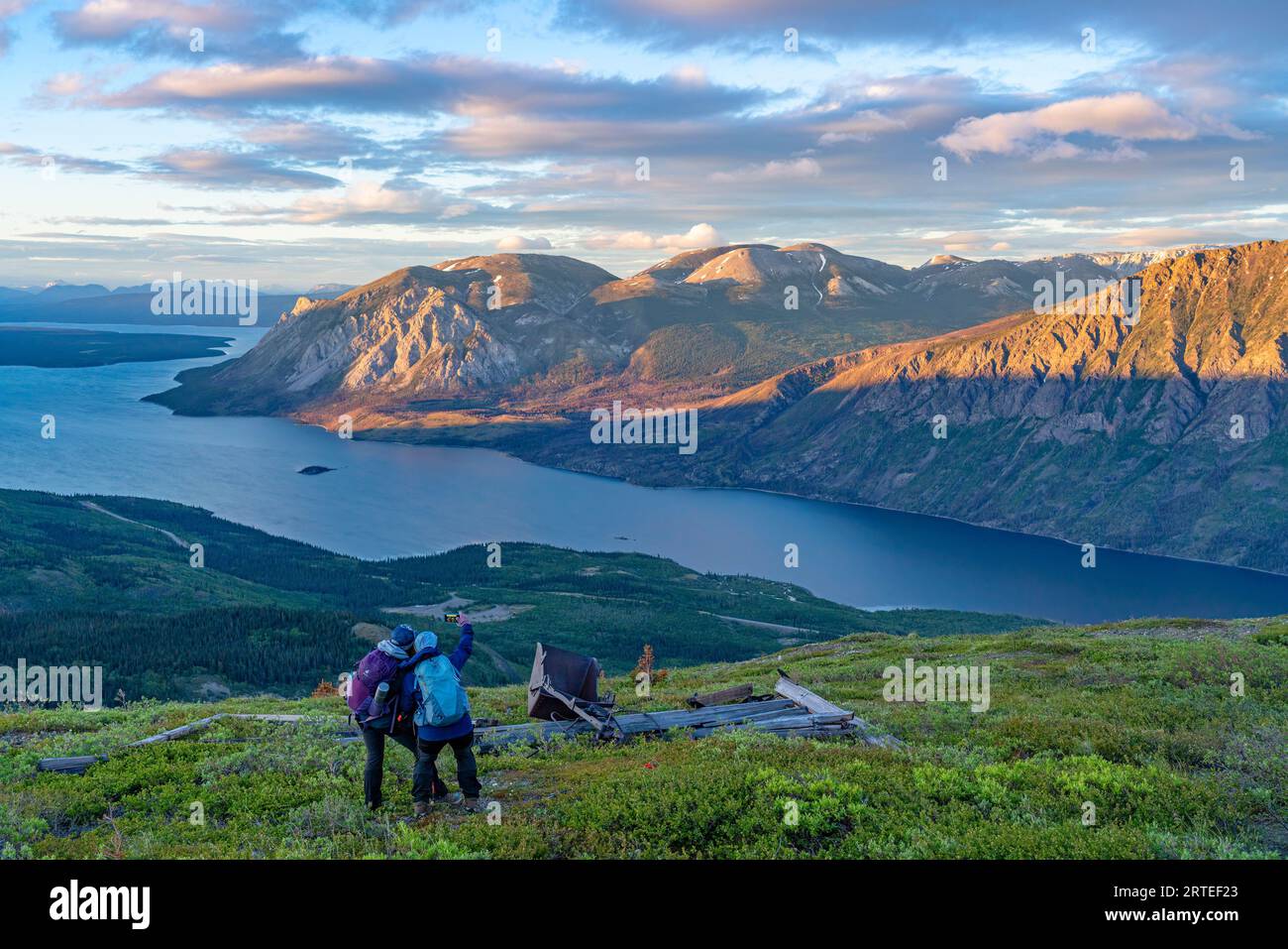 Blick von hinten auf zwei Frauen, die auf einem Berggipfel stehen und die Aussicht genießen und ein Selfie machen, während Sie die erstaunliche... Stockfoto