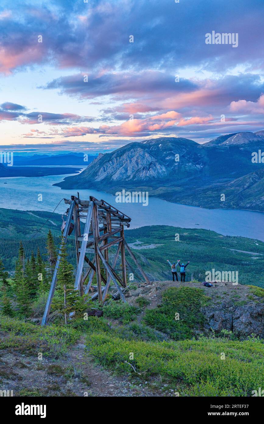 Zwei Frauen stehen auf einem Berggipfel neben einem Bergbaureliquium auf dem Montana Mountain, mit erhobenen Armen in der Luft, um zu feiern, und genießen den Wettbewerb... Stockfoto