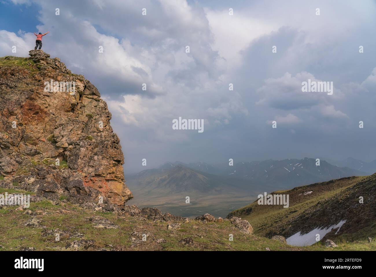 Frau, die auf dem Surfbird Mountain entlang des Dempster Highway steht, während sich in der Ferne Gewitterwolken sammeln, erreichte die Siegesposition Stockfoto