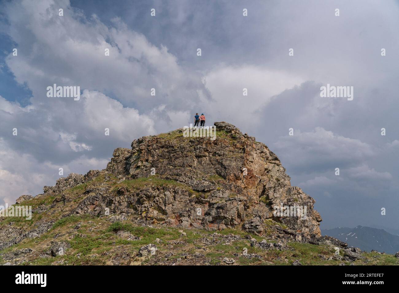 Zwei Frauen, die auf einem Berggipfel am Dempster Highway stehen und auf die in der Ferne aufgebrühten Sturmwolken blicken, Yukon Territory, Kanada Stockfoto