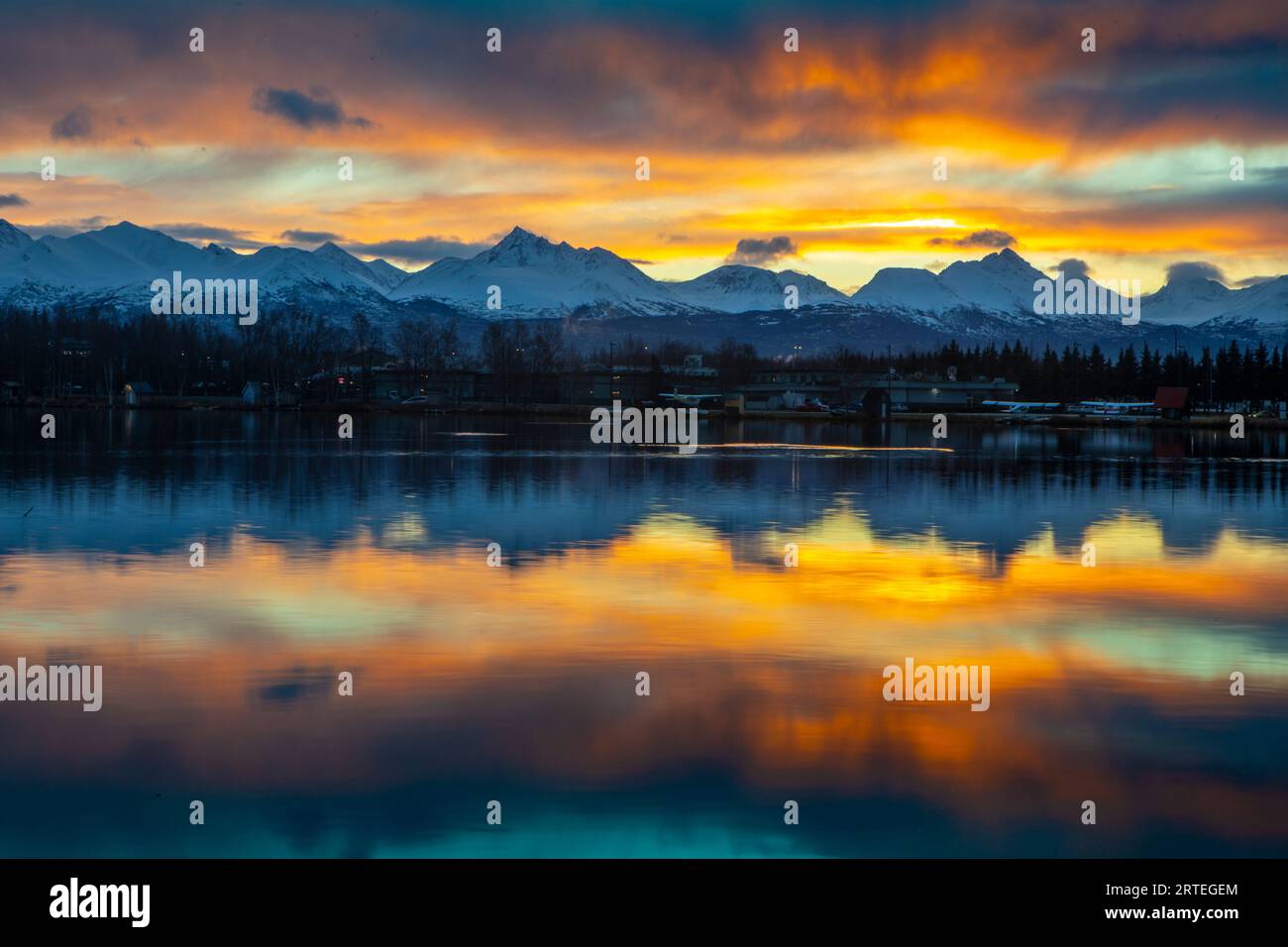 Sonnenaufgang im Spätherbst, früherer Wintertag reflektiert auf dem Spenard-See, mit Wasserflugzeugen im Schatten und schneebedeckten Chugach Mountains im Jahr ... Stockfoto