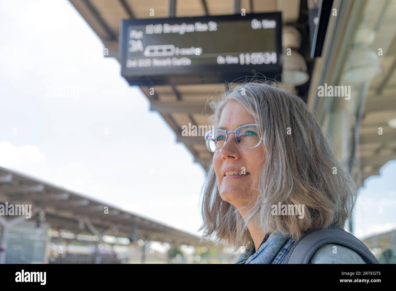 Reife Frau, die an einem Bahnhof wartet; Großbritannien Stockfoto