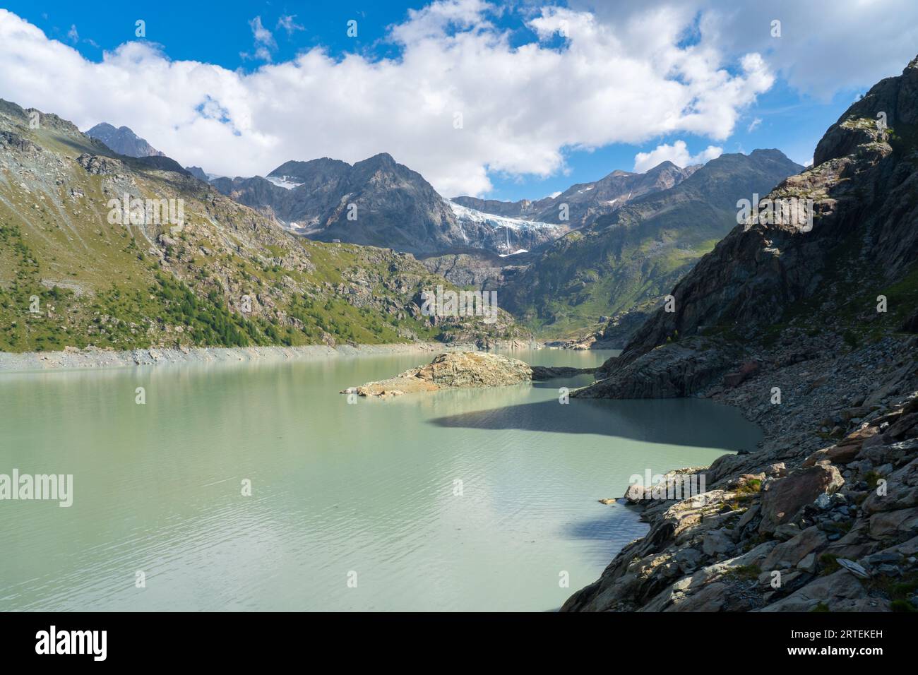 Alpe Gera See und Fellaria Gletscher mit Wasserfall im Hintergrund, blauer Himmel mit Wolken, sanftes warmes Licht. Berglandschaft Stockfoto