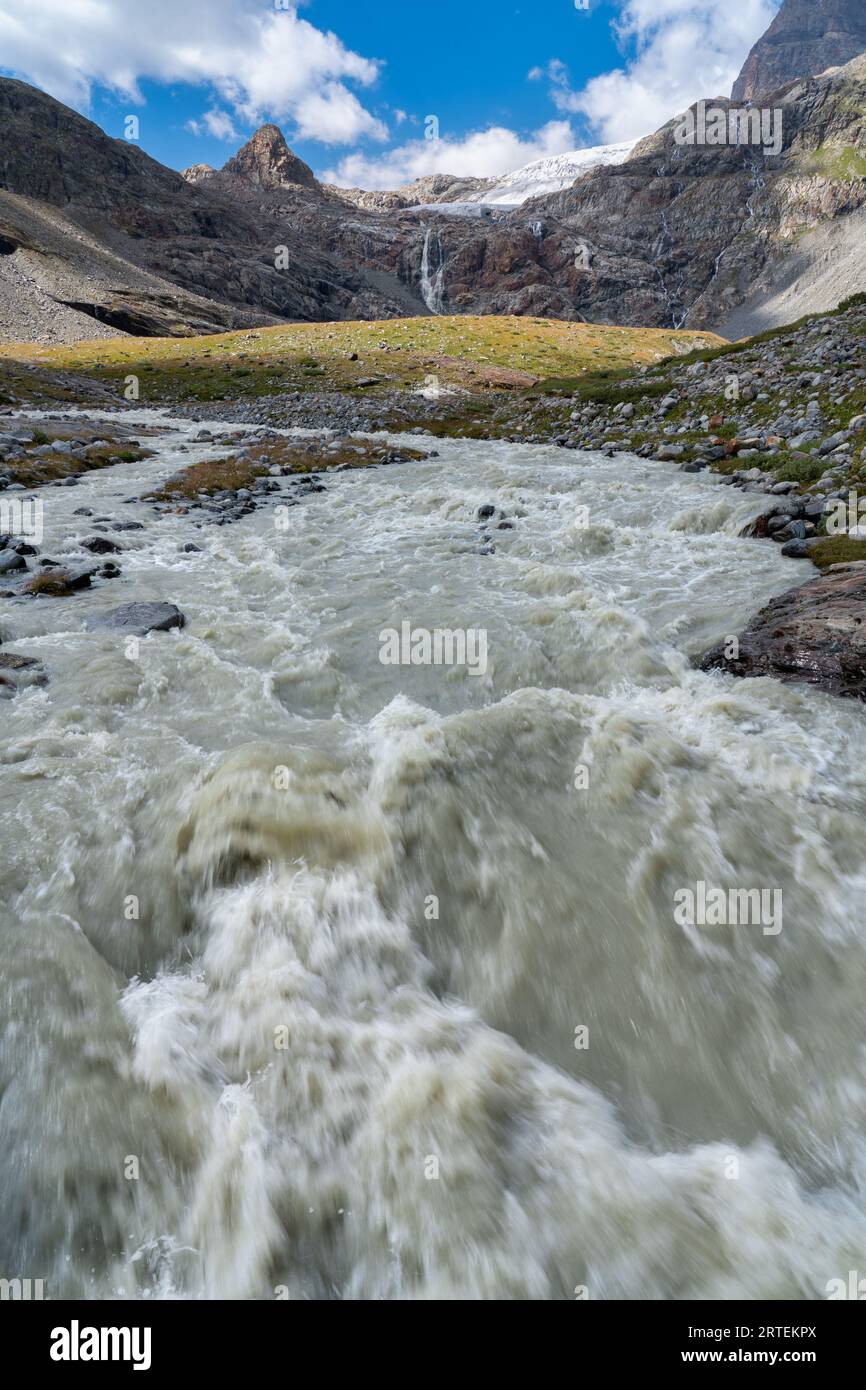 Fellaria-Gletscher und Wasserfall im Hintergrund, blauer Himmel mit Wolken, Wasser lange Exposition des Gebirgsbaches vorne. Bernina Massif. Stockfoto