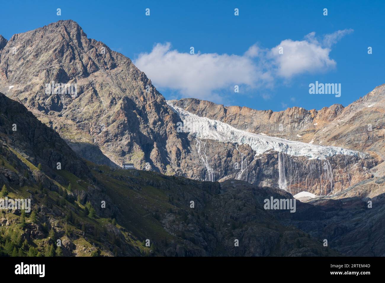Bignami-Hütte und Fellaria-Gletscher mit Wasserfall im Hintergrund, felsiger Gipfel mit weichem warmem Licht, blauer Himmel mit Wolke. Valmalenco-Landschaft Stockfoto