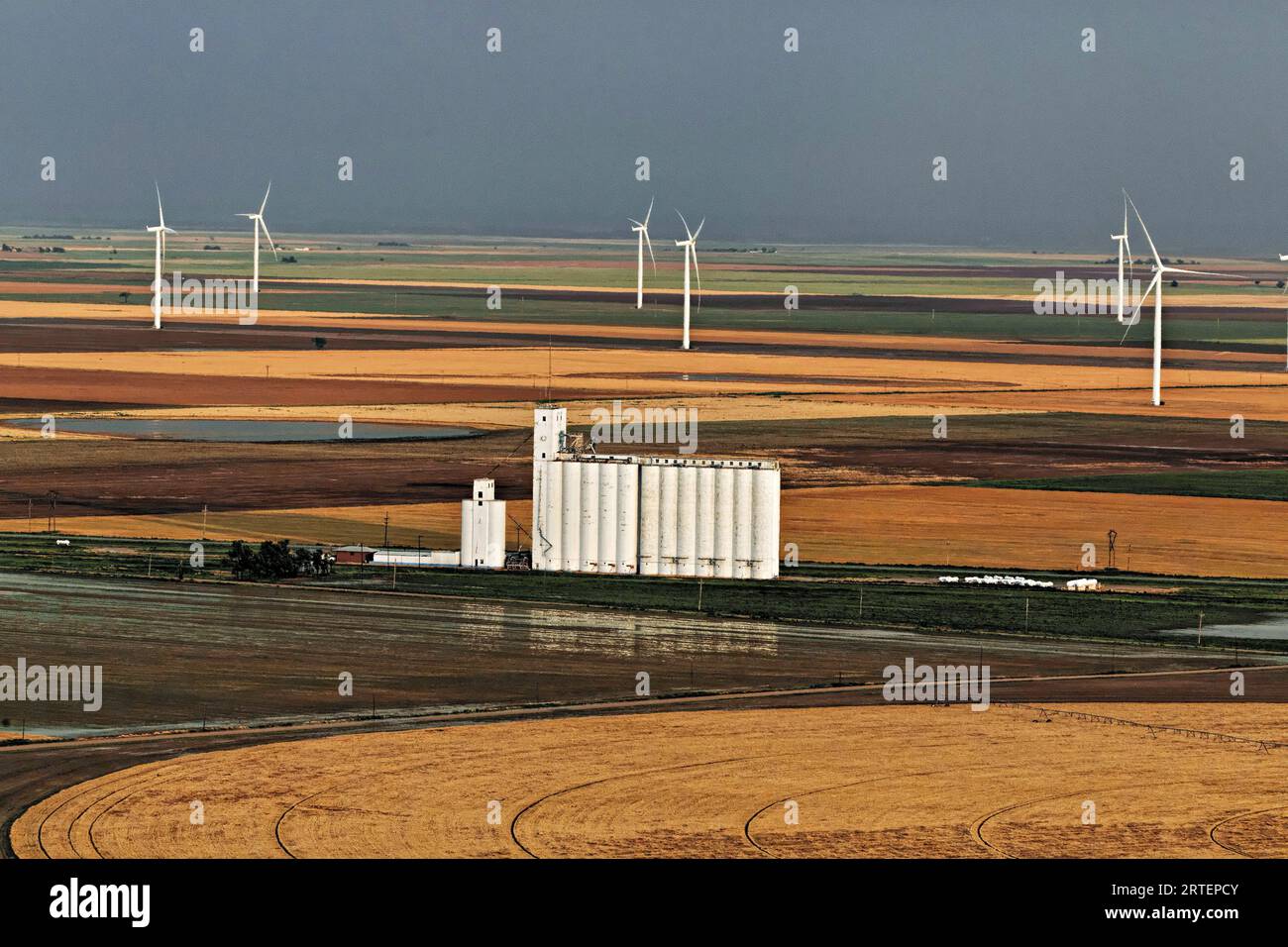 Windturbinen in Kansas bilden die Kulisse für den Getreideaufzug auf landwirtschaftlichen Feldern. Windstrom versorgt den Staat mit fast der Hälfte seines Stroms Stockfoto