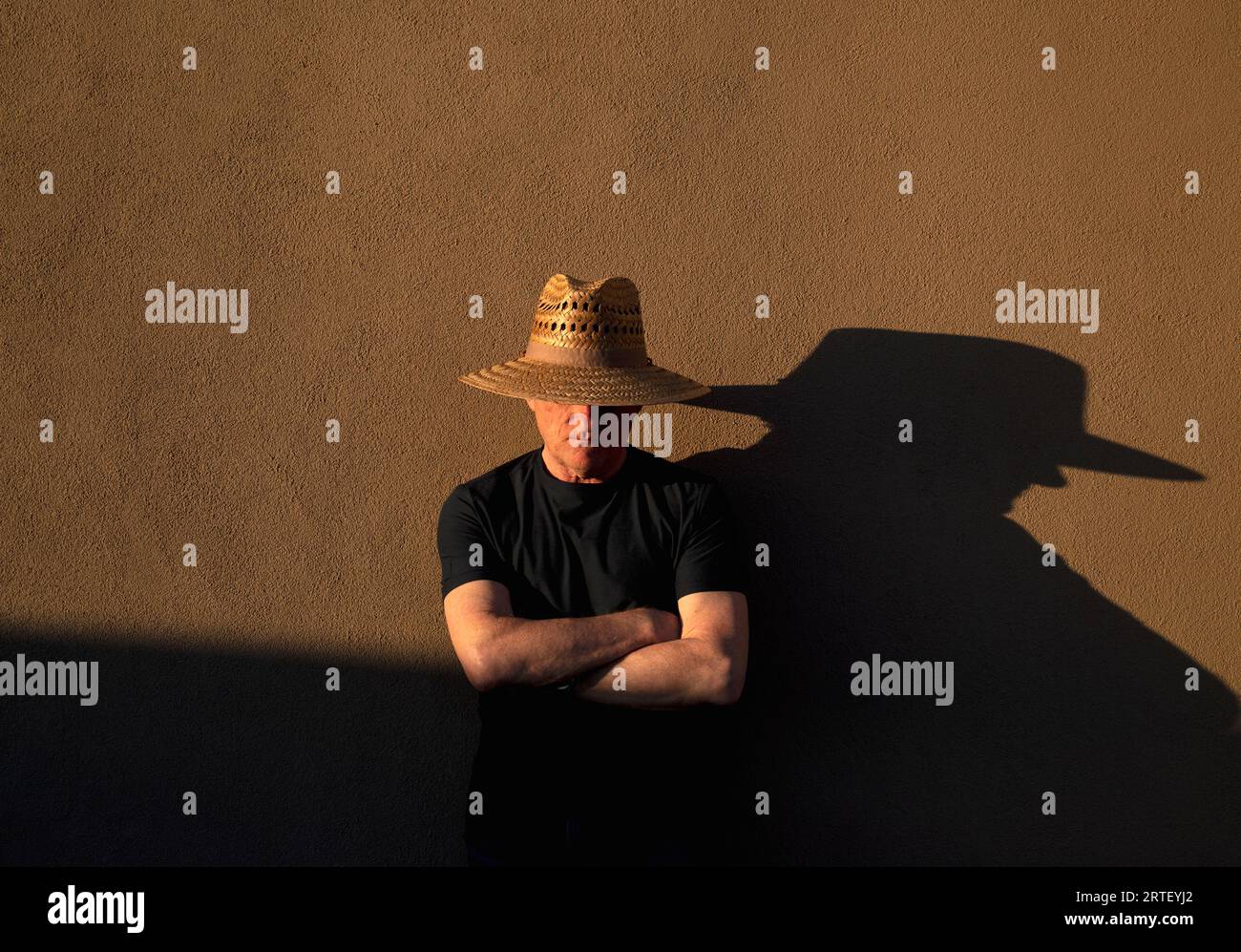 Senior Mann mit Strohhut, der Schatten an die Wand wirft Stockfoto