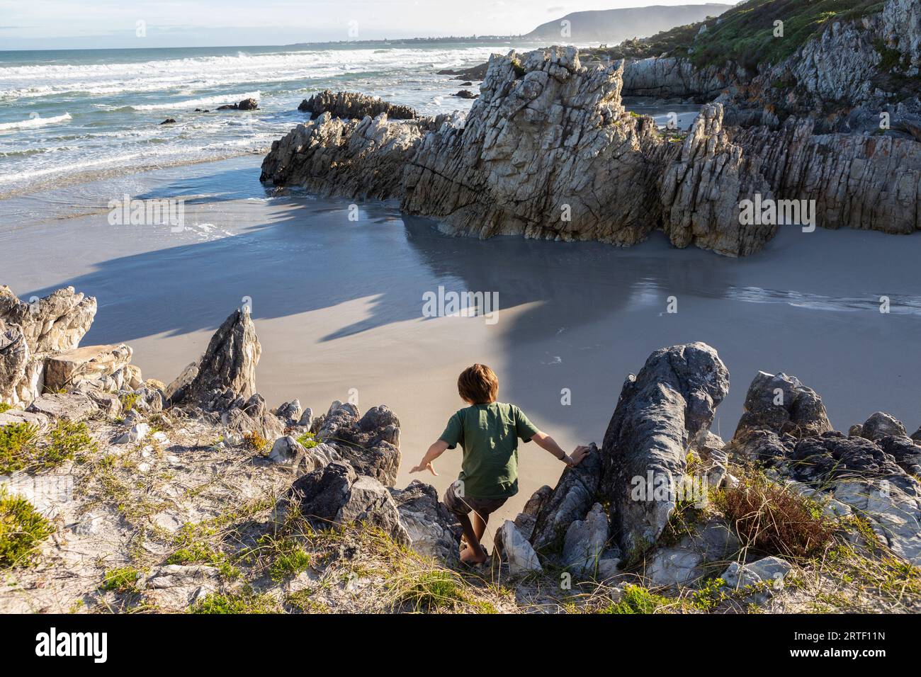 Südafrika, Hermanus, Boy (10-11), die felsige Küste am Voelklip Beach erkunden Stockfoto