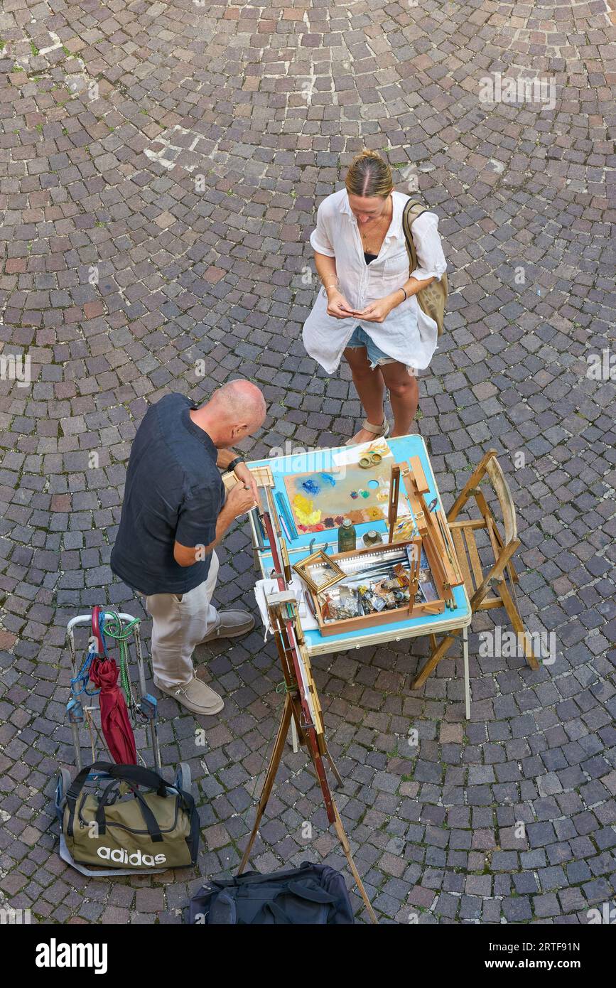 Die Feriengäste in der Altstadt von Malcesine in Italien kauft ein bemaltes Bild eines Straßenkünstlers als Souvenir Stockfoto