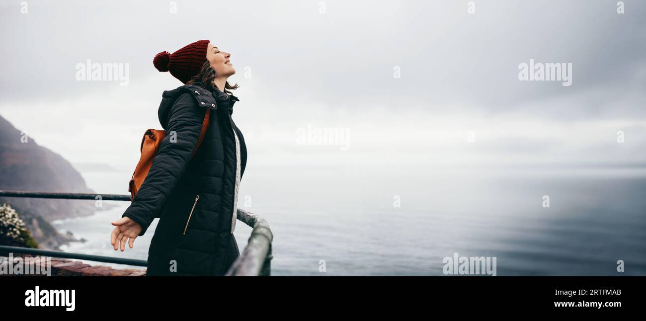 Rucksacktouristin mit Wanderlust, die nach dem Wandern mit ihrem Rucksack draußen auf einer Küstenklippe steht. Solo-Reise- und Abenteuerkonzept. Die Stockfoto