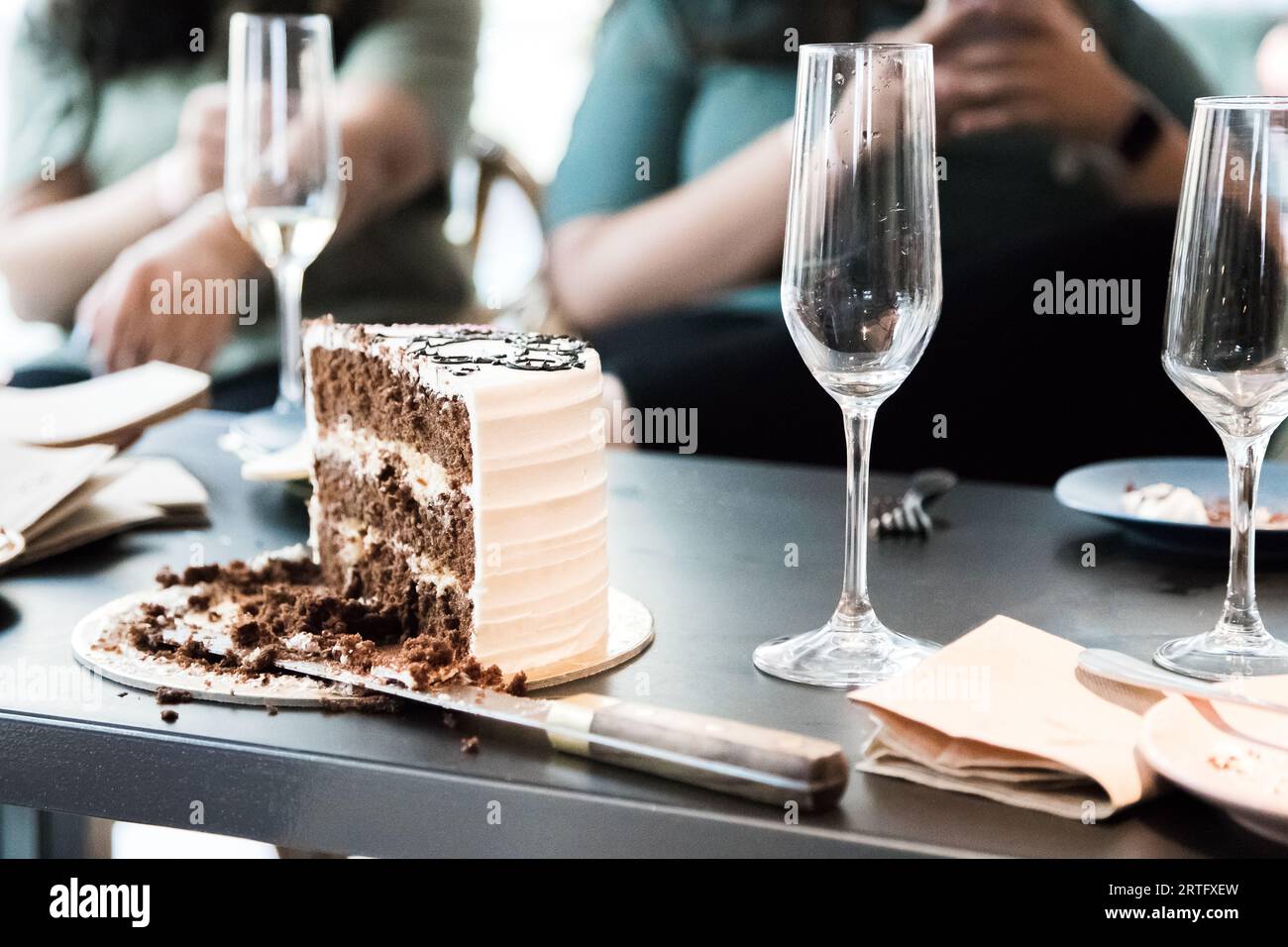 Junggesellenabschied. In Scheiben geschnittener ​​chocolate-Kuchen und Gläser Champagner auf dem Tisch mit verschwommenen Menschen im Hintergrund. Nahaufnahme Stockfoto