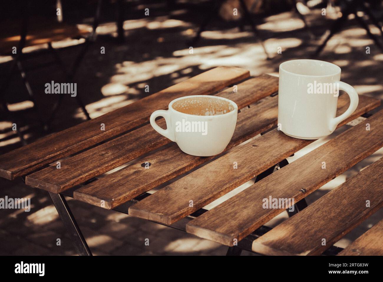 Zwei leere Kaffeetassen auf Holztisch. Frühstückstisch. Kaffeemöbel auf dem Bürgersteig. Getränke am Morgen. Cappuccino in weißen Tassen. Tägliche städtische Lebensweise. Stockfoto