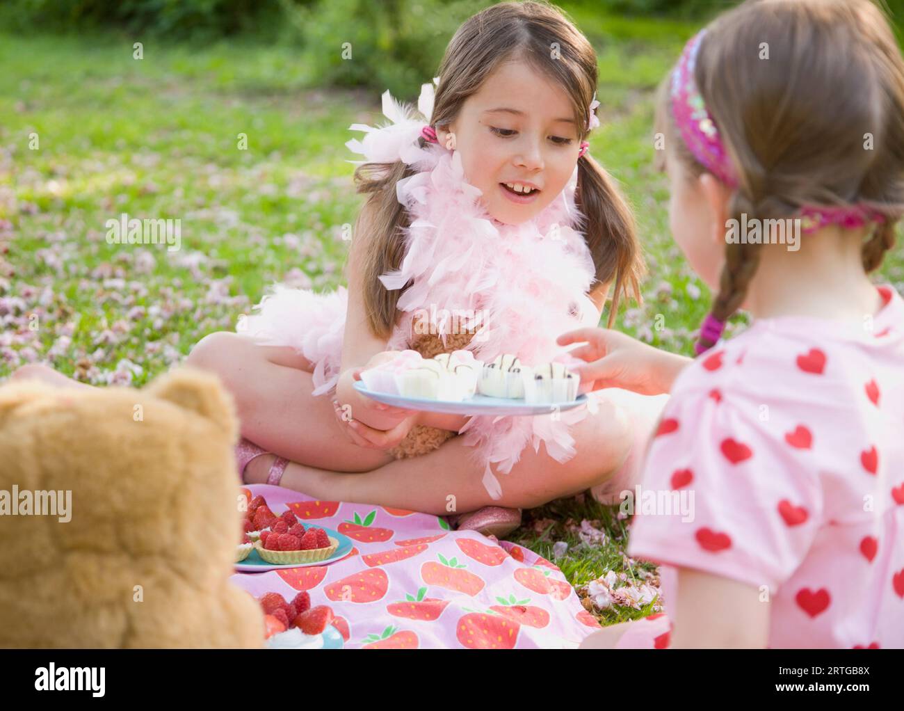 Junge Mädchen sitzt im Garten Rasen trägt eine rosa Federboa mit Cupcakes an einen Freund Stockfoto