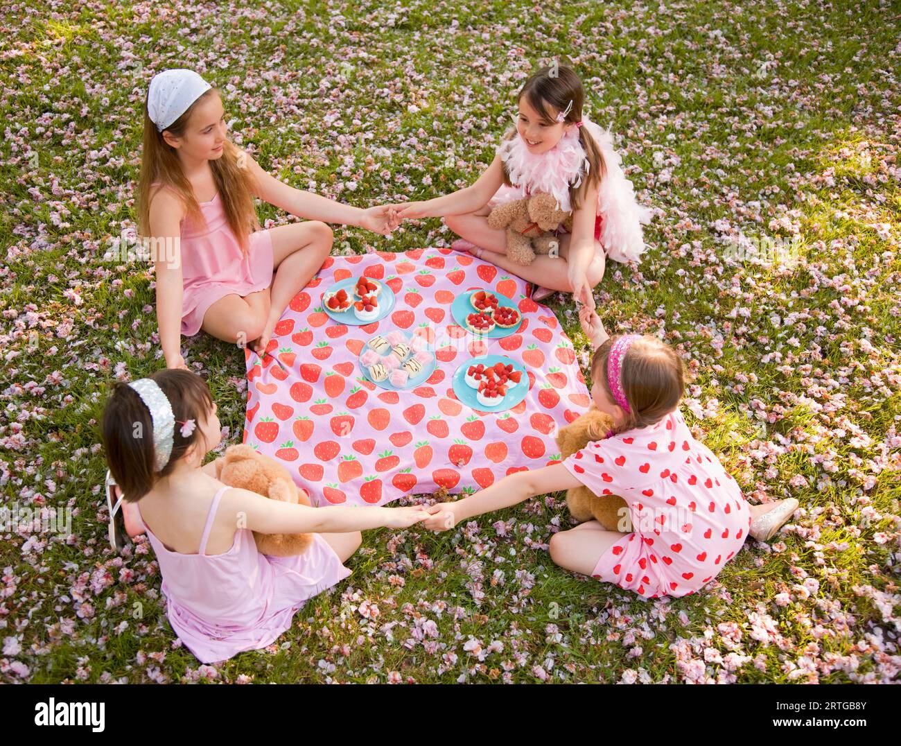 Vier junge Mädchen, die um eine bunte Decke sitzen und Hände halten und eine Party feiern Stockfoto
