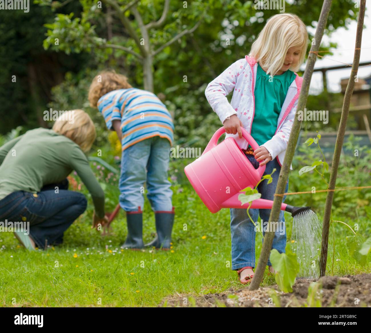 Junge blonde Mädchen stehen und Bewässerung von Pflanzen mit rosa Gießkanne Stockfoto