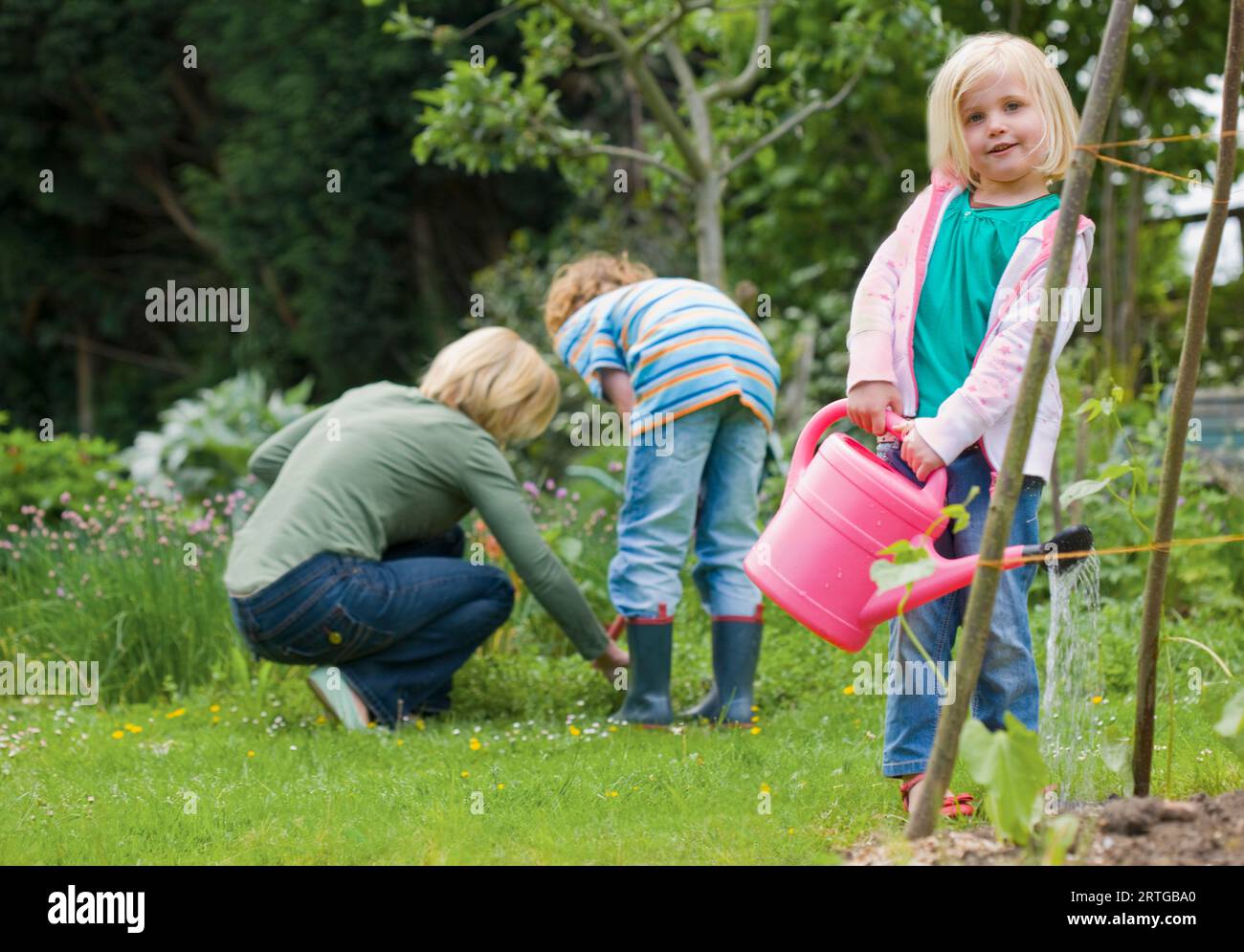 Junge blonde Mädchen stehen und Bewässerung von Pflanzen mit rosa Gießkanne Stockfoto